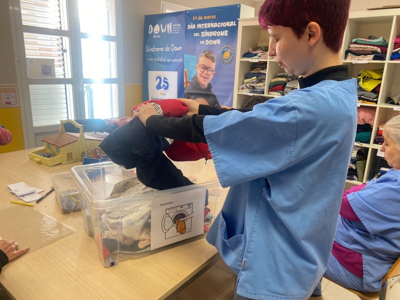 Recibiendo los articulos, la compañera de pie, saca de una caja las prendas recibidas.